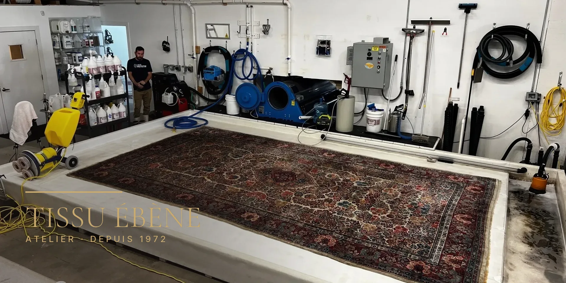 Grand tapis d&rsquo;Orient &agrave; m&eacute;daillon &eacute;tendu sur une table de lavage dans un atelier &eacute;quip&eacute; de machines