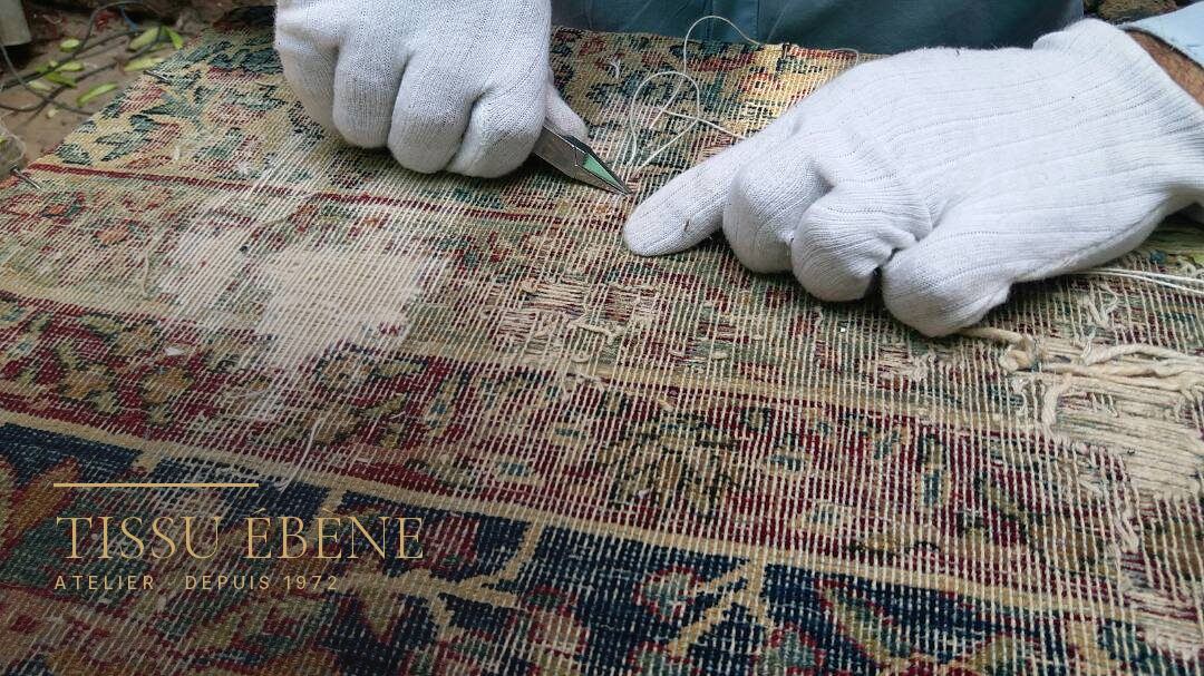 Mains gant&eacute;es tenant une pince sur un tapis us&eacute; jusqu&rsquo;&agrave; la trame, d&eacute;cor floral rouge et bleu
