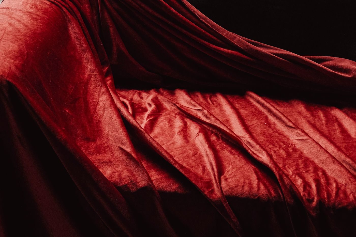 Drapé de velours rouge profond aux plis souples sous une lumière rasante