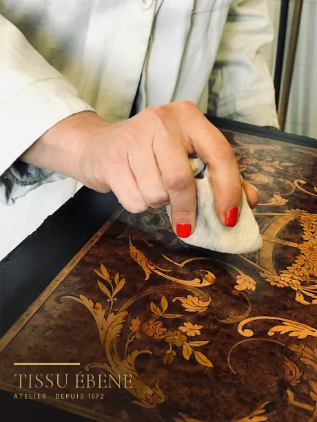 Main polissant au tampon le plateau marqueté d’un meuble ancien