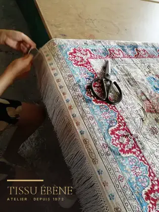 Franges d'un tapis en soie refaites à la main, fil à fil, sur la table de l'atelier